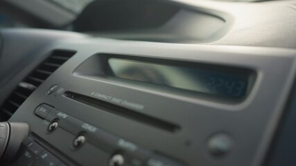 close up of dashboard showing stereo control panel and cd display screen blinking inside parked car under daylight with visible air vent and buttons around media console