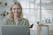 © polack - Portrait of beautiful blogger woman is sitting at a desk with a laptop in front of her, she is smiling and looking on camera