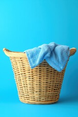 Poster - Wicker laundry basket filled with a soft blue towel against a vibrant blue background creating a clean and fresh aesthetic in a simple studio shot