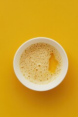 Poster - Top view of frothy yellow beverage in a white bowl against a vibrant yellow background creating a warm and inviting visual with a minimalist aesthetic and a modern style