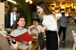 © JackF - European woman holds a menu in her hands and orders food from a waitress in a restaurant. Smiling female waitress taking order in cozy restaurant with warm lighting