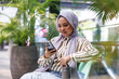 © Jovo Jovanovic/Stocksy - Happy young woman in hijab using smartphone on bench