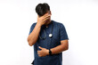 © ArvStd - Indoor portrait of handsome doctor man, wearing medical uniform, making face palm gesture while smiling, standing over white background amazed with stupid situation.
