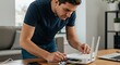 © SimpleDesignStudio - A focused white male in his 30s connects cables to a white Wi-Fi router on a wooden desk in a home or office setting, ensuring internet connectivity.
