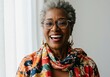© SimpleDesignStudio - Portrait of a joyful older Black woman with grey hair and glasses, wearing a vibrant floral scarf, smiling broadly and looking at the camera.