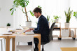 © Studio Marmellata - A businessman in a suit works on his laptop at a wooden desk in a bright, modern office. Plants add a touch of nature to the workspace.