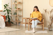 © Pixel-Shot - Young woman sitting in armchair and reading book in living room