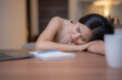 © Tj - Young Asian businesswoman sleeping at her desk, exhausted from long hours of working on her laptop at home. Feeling the weight of stress and fatigue after meeting tight deadlines