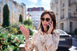 © Nick ALDI - A beautiful woman in a light dress in summer is walking down the street talking on the phone on the background of the city.
