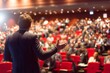© Graini - Speaker addressing a large audience at a conference or seminar event