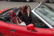 © Viktar - A woman is casually sitting inside a vibrant red convertible car while engaging in a conversation on her cell phone at the same time