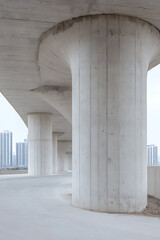Poster - Concrete pillars support an elevated structure with skyscrapers visible in the background, creating a modern architectural scene.