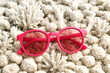 © Arttali_Neuro - Bright pink sunglasses with tinted lenses placed on white coral stones and reef pieces, summer, beach vibes. Concept of global warming and the death of corals, ignoring the problem