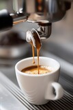 At the moment of serving espresso coffee, very hot in a white cup. Served with a coffee machine in a restaurant. The coffee comes out of the nozzle of the coffee machine. 