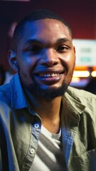Poster - Vertical Video Portrait of african american person smiling and working in his living room, using laptop to solve remote freelancing tasks as a self employed guy. Young adult feels relaxed at home