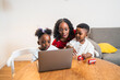 © Koldo_Studio - African mother and children enjoying time together, looking at a laptop, playing with toy cars, in a cozy home environment
