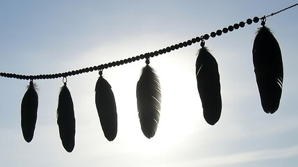 Poster - Silhouette of five feathers hanging from a string against a bright sky. The feathers are dark and create a contrast with the light background. The image evokes a feeling of peace and simplicity