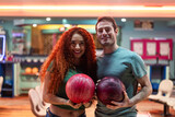 Happy couple holding bowling balls in bowling alley