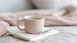 © Nice Seven - A beige coffee mug, a silver pen, and an open notebook rest on a soft bed, creating a cozy and relaxed morning scene, Mindful Product Photography.