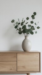 Aufkleber - A stylish minimalist sideboard made of light wood highlights the serene aesthetic of the room. A ceramic vase sits atop, elegantly showcasing fresh green eucalyptus leaves for a touch of nature