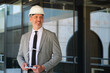© Ladanifer - Smiling engineer holding small wind turbine model wearing hardhat in front of modern glass building