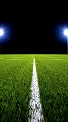 Poster - A vivid soccer field under stadium lights at night, showcasing vibrant green grass with a white stripe leading towards the horizon. The contrasting dark sky enhances the illuminated ambiance, creating