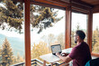 © Davor - Man working remotely on laptop with mountain view from cabin office