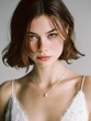 ©  Mariya Primakina - Portrait of a young bride with a bob hairstyle and a simple necklace looking straight into the camera on a light gray background.