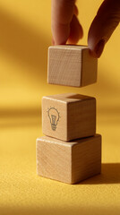 Poster - Three light-brown wooden cubes stacked, one with a lightbulb icon, on a yellow surface, symbolizing idea generation, innovation, or problem-solving