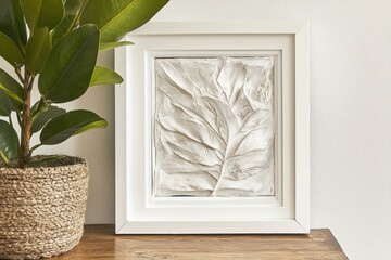 Poster - Serene interior showcasing a framed plaster leaf art piece alongside a vibrant potted plant on a wooden surface capturing a tranquil and artistic ambiance