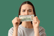 © Pixel-Shot - Upset young woman with dollar banknote on green background, closeup