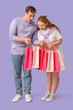 © Pixel-Shot - Beautiful young couple with pink shopping bags on lilac background