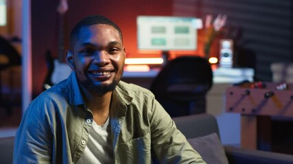Poster - Portrait of black freelancer laying on the sofa and texting on phone, relaxing and smiling in his modern loft. Man solving daily teleworking tasks from the living room with cool lights. Camera B.