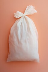 Poster - Simple White Muslin Bag Tied with a Bow on a Soft Peach Background for Product Packaging
