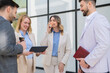 © Dexon Dee - Group of business professionals enjoying a casual break with coffee and a tablet outside a modern office building.