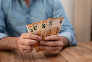 Poster - Male entrepreneur holds euro banknotes in hands carefully counting money to pay landlord for expensive rental services of office space sitting at wooden table