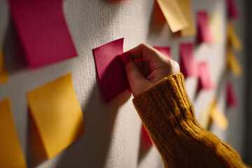 Aufkleber - Close-up of hand placing red sticky note on textured wall, surrounded by yellow and red notes.  Shows planning, organization, or brainstorming concept