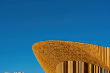 Poster - Modern, curved yellow building with striped pattern set against a clear blue sky, showcasing unique architectural design.