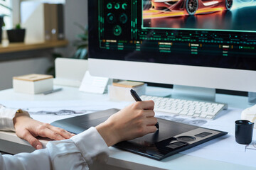 unrecognizable female graphic designer sitting in office in front of computer, drawing using tablet 