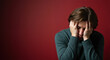 © NN AI - Distressed young man covering face with hands against red background. Person in green sweater showing signs of despair. Mental health crisis and emotional suffering concept. Depression awareness.