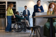 © Aida - Diverse business team enjoying coffee break in modern office, including a disabled colleague