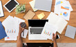 © Prostock-studio - Office workspace top view. African-american businessman working at wooden desk, using laptop and various objects all around
