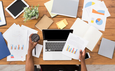 Poster - Office workspace top view. African-american businessman working at wooden desk, using laptop and various objects all around