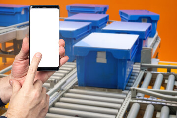 Poster - Conveyor technologies. Phone with blank screen in hands. Plastic boxes on conveyor. Production line with blue containers. Mock up smart phone. Conveyor control concept via mobile app