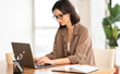 © Prostock-studio - Pensive Worker. Portrait of smiling girl in eyeglasses using laptop, sitting at office and doing research, copyspace