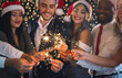 © Prostock-studio - Merry Christmas greeting card. Group of happy friends in New Year eve with sparkling bengal lights, closeup