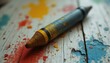 © Tanya - Close-up of a blue and yellow crayon lying on a rustic paint-splattered surface, showcasing artistic texture and color