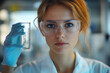 © Sofia - Woman in lab coat holding test tube with colorful liquid, surrounded by scientific equipment in a well-lit laboratory setting.