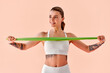 © HBS - A young woman in white fitness clothing performing an arm exercise with a resistance band against a soft peach background. Concept: fitness, training, motivation.