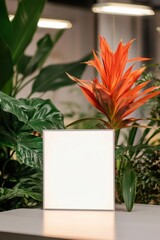 Poster - Blank square frame mockup on white table surrounded by green tropical plants and orange flower in bright modern interior